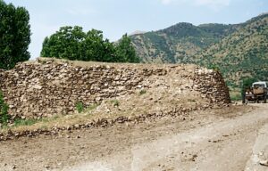 Diyarbakır-Bitlis kervan yolu üzerinde bulunan tarihi Şeyh Ciman Hanı kalıntılarının, 1972 yılına ait siyah-beyaz fotoğrafından aslına uygun olarak renklendirilmiş hali. Ön planda taş duvar kalıntıları ve toprak yol, sağda dönemin bir kamyoneti, arka planda ise ağaçlar ve dağlık arazi görünmektedir.
