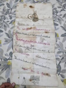 Kocakaplan Köy Konağı, Berat; Tuğranın Okunuşu: Abdülhamid Han bin Abdülmecid, el-muzaffer daima 1) Nişân-ı şerîf-i âlî-şân-ı sâmî mekân-ı sultânî ve tuğrâ-yı garrâ-yı cihân-ı hakānî sâmi oldur ki 2) Nezâret-i Evkâf-ı Hümâyûn-ı mülükâneme mülhâk Evkaftan Viranşehir kazasına tabi Kapucılar karyesinde kâ’in Hüseyin Çavuş Câmi’i şerifinde 3) Yevmî bir akçe vazife ile hitâbet cüz’ünün tevcîhine dâ’ir vârid olan inhâ üzerine kaydı bilâ-hurûc mu‘âmele-i kalemiyesi lede’l-icrâ cihet-i mezkûre mutasarrıfı 4) Ahmed bin Es-seyyid Hüseyin’in fevtiyle mahlûlünden ve sulbî kebîr mahdumları Hüseyin ve Tahir ve Mehemmed … adem-i ehliyetlerinden bi’l-imtihân ehliyeti nümâyân olan İsmail bin Ahmed zîde salahahuya Mahkeme-i …. İ‘lâmı mûcebince bilyevm 5) yedine berât-ı âlişânım i‘tâ olunmak bâbında cânib-i nezâret-i evkāf-ı hümâyûnumdan bâ-telhîs lede’l-arz şeref-sünûh ve sudûr iden hatt-ı hümâyûn-ı şevket-makrûn-ı şâhânem mûcebince 6) hitâbet-i mezkûre mûmâ-ileyhe tevcîh olunmağın bin iki yüz bir senesi cemaziyelevvelinin on on beş … … bu Berât-ı Hümâyunu 7) virdim ve buyurdumki mûmâ-ileyh zikrolunan hitâbet cihetine vazîfe-i mersûmesiyle mutasarrıf olub edâ-yı hüsn-i hizmet ile şöyle bileler alâmet-i şerîfeme 8) i‘timât kılalar tahrîren yevmü’s-sâbi‘-aşer min şehr-i cemaziyelahir sene ihda ve selase-mie ve elf (17 Cemaziyelahir 1301) [M. 14 Nisan 1884] Evkâf-ı Hümâyun-ı Hazîne-i Celîlesine mahsus Berât-ı Âlişân yazılmak içün varakadır Yalnız beş guruşdur. Okuyanlar: Ahmet Coşkun Hasibe Durmaz Cengiz Elmas Şenay Kocakaplan Şeyma Erden
